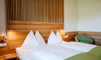 A modern bedroom with two single beds and wood details. The soft lighting creates a cozy atmosphere.