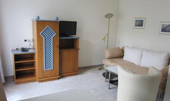A modern living room with a couch, a television, and a wooden cabinet. The walls are painted light and there are decorative pictures.