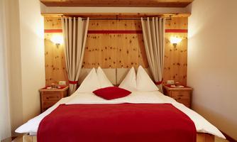 A cozy bedroom with a large bed and wooden paneling. The red accents and soft lighting create an inviting atmosphere.