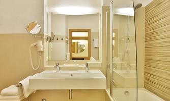 A modern bathroom with a sink, mirror, and a shower. The walls are bright and the furnishings are kept minimalist.