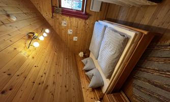 A cozy bedroom with wooden paneling and a double bed. There are two nightstands and a window with curtains.