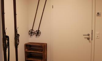 A hallway with carved wooden walls and a ceiling light. Two skis hang on the wall, and on the right, there is a wooden shelf.