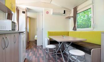 A modern and bright motorhome with a cozy seating area and a table. The kitchen is well-equipped, and the space has large windows that let in a lot of light.