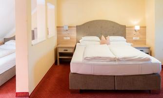 A comfortable hotel room with a large double bed and two bedside tables. The walls are painted in soft colors and there is a pleasant red carpet.