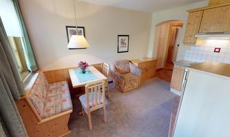 A cozy living area with a dining corner and comfortable seating. The bright colors and wooden details create an inviting atmosphere.
