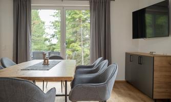 A modern dining area with a large table and comfortable chairs. Large windows provide plenty of daylight and a view of nature.