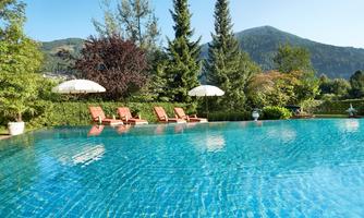 A beautiful pool with clear blue water and sun loungers. In the background, green trees and mountains can be seen.