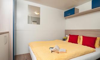 A cozy bedroom with a large bed and bright yellow bedding. On the wall, there are blue shelves and a mirror.