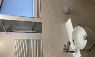A modern bathroom with a round sink and elegant fixtures. In the background, a shower and a towel rack can be seen.
