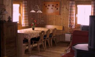 A cozy dining area with a wooden table and chairs. Walls made of wood and large windows create an inviting atmosphere.