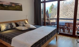 A bright bedroom with a large bed and wooden furniture. A view of a terrace and the garden through the windows.