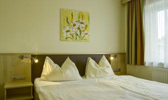 A cozy bedroom with a large bed and two pillows. A painting with floral motifs hangs on the wall.