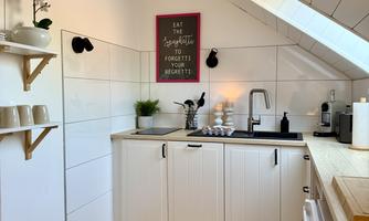 A modern kitchen with white cabinets and wooden details. On the wall hangs a decorative sign with a message.