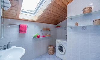 A modern bathroom with a washing machine and shelves. Bright tiles and a skylight create a pleasant atmosphere.