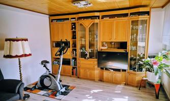 A cozy room with a wooden bookshelf and a television. In the corner stands an exercise bike and a plant arrangement provides a fresh atmosphere.