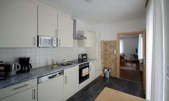 A modern kitchen with white cabinets and a countertop. In the background, another room is visible.