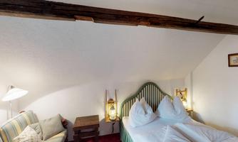 A cozy bedroom with a double bed and two pillows. Lantern-like light sources hang on the wall, and there is a comfortable seating area.