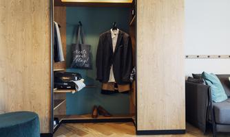 A modern wardrobe with a blue suit and a bag. In the background, a luggage rack and a cozy seating area can be seen.
