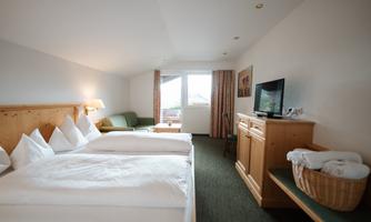 A cozy hotel room with two beds and a small sofa. The room has a window with a view outside and a wooden dresser with a television.