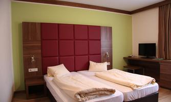 A simple room with two single beds and a red upholstered wall. There is a workspace with a television and a wooden desk.