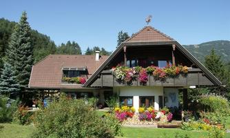 A beautiful house with a green garden and colorful flowers. The architecture is traditional with a sloping roof and a stylish balcony.