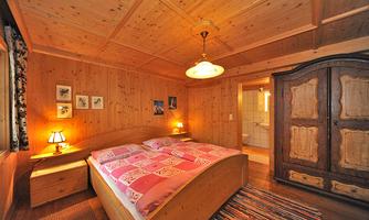 A cozy bedroom with wood paneling and a large bed. The walls are decorated with pictures, and a stylish wardrobe is in the room.