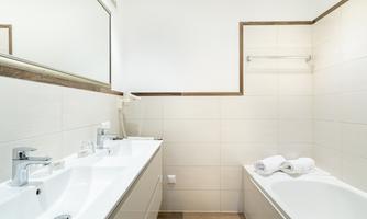 A modern bathroom with a sink and a bathtub. Fresh towels and a large mirror are visible.