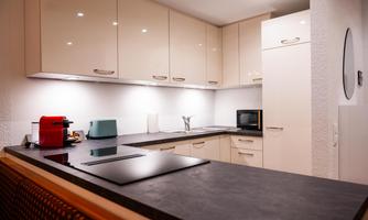 A modern kitchen with white cabinets and a dark countertop. There is a refrigerator, a microwave, and a coffee maker on the counter.