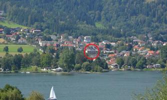 A picturesque view of a lake with a small sailing yacht. In the background, houses and mountains can be seen.