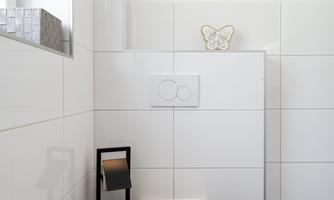 A modern toilet in a bright, tiled bathroom. The walls are white and there is a small windowsill with decoration.