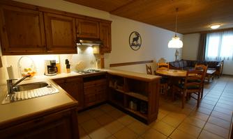 A bright kitchen with wooden cabinets and modern appliances. In the background, there is a dining area with a table and chairs.