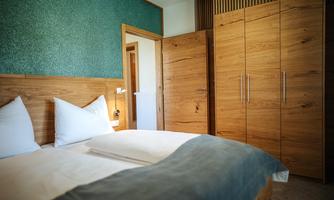 A cozy bedroom with two beds and modern wooden furniture. The walls are painted in soft colors, creating a relaxed atmosphere.