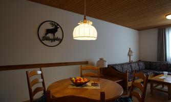 A cozy dining area with a wooden table and chairs. On the wall hangs a decoration featuring a deer, and the lamp provides warm light.