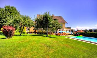 A beautiful garden with well-maintained lawn and trees. In the background, there is a large house with a pool.