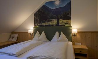 A cozy bedroom with a large bed and two pillows. An impressive landscape picture hangs on the wall, depicting mountains and sunshine.