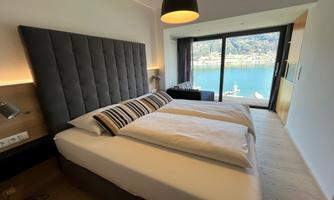 A modern bedroom with two beds and a large window that offers a view of the countryside. The decor is bright and inviting.