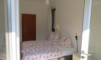 A bright bedroom with a large bed and floral bedspreads. There is a window and a covered door that opens the space.