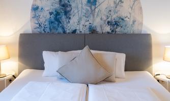 An elegant bedroom with a gray headboard and a piece of art in blue and white above the bed. Next to the bed, there are two bedside lamps that create a cozy atmosphere.