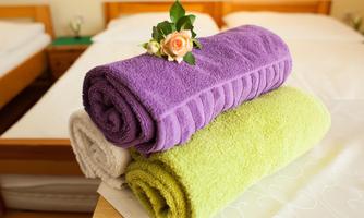 Colorful towels in purple, green, and white are lying on a table. A small bouquet of roses decorates the top roll.
