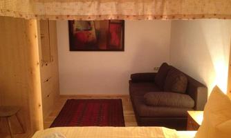 A cozy bedroom with a bed and a gray couch. A modern artwork hangs on the wall, and the floor is covered with a carpet.