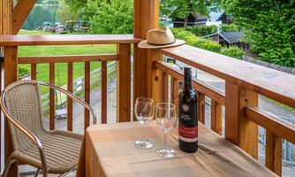 A cozy balcony with a view of a lake. On the table are a bottle of wine and two glasses.