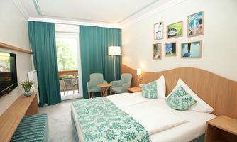 A modern hotel room with a large double bed and a stylish décor. There are cozy seating areas and large windows that let in plenty of light.
