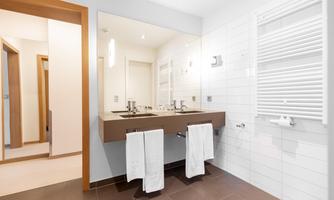 A modern bathroom with two sinks and large mirrors. Bright tiles and towels in white complete the elegant design.