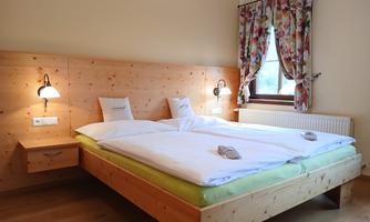 A cozy bedroom with a double bed and wood-paneled walls. The windows are adorned with colorful curtains, and there is soft lighting next to the bed.
