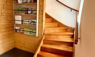 A wooden staircase leads up to a bright room. A display stand with flyers hangs on the wall.