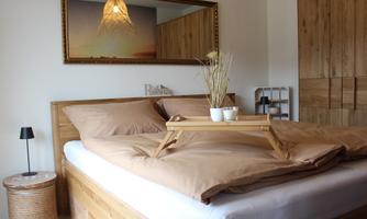 A stylish bedroom with a large bed and beige bed linens. A wooden mirror and an elegant table lamp complement the cozy atmosphere.