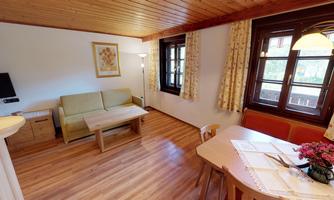 A cozy living area with a sofa and a table. Large windows let in plenty of light and the walls are paneled with wood.