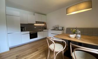 A modern kitchen with white cabinets and hardwood flooring. On the table, there is a vase with flowers and two chairs.