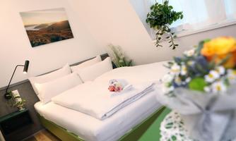 A modern bedroom with a large bed and fresh flowers. A picture of a landscape hangs on the wall, and there are plants that make the room cozy.