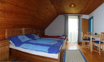 A cozy bedroom with a wooden roof and two beds. There is a table with chairs and windows looking outside.